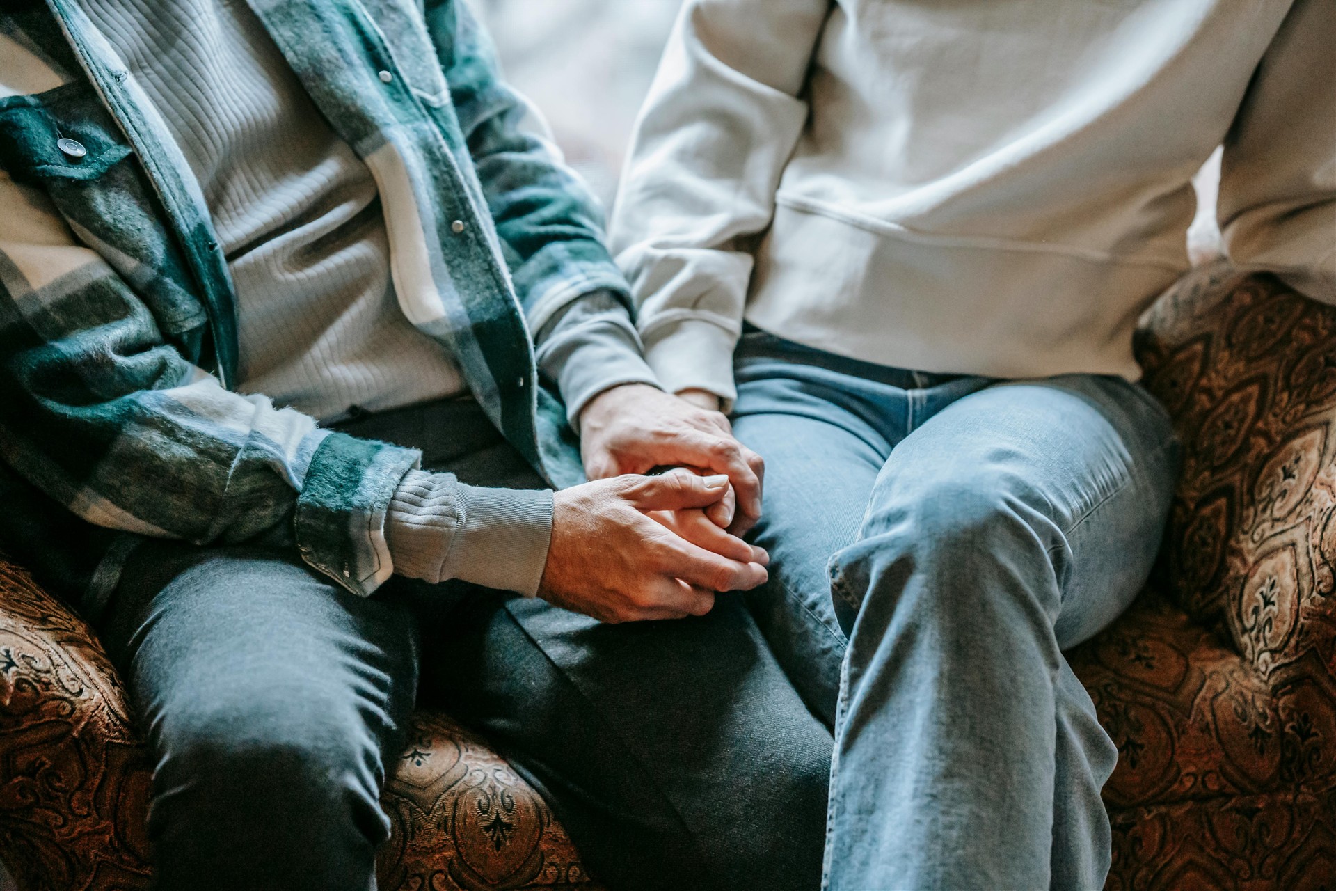 to som sitter og holder hender i ensofa. ansikt er ikke synlig